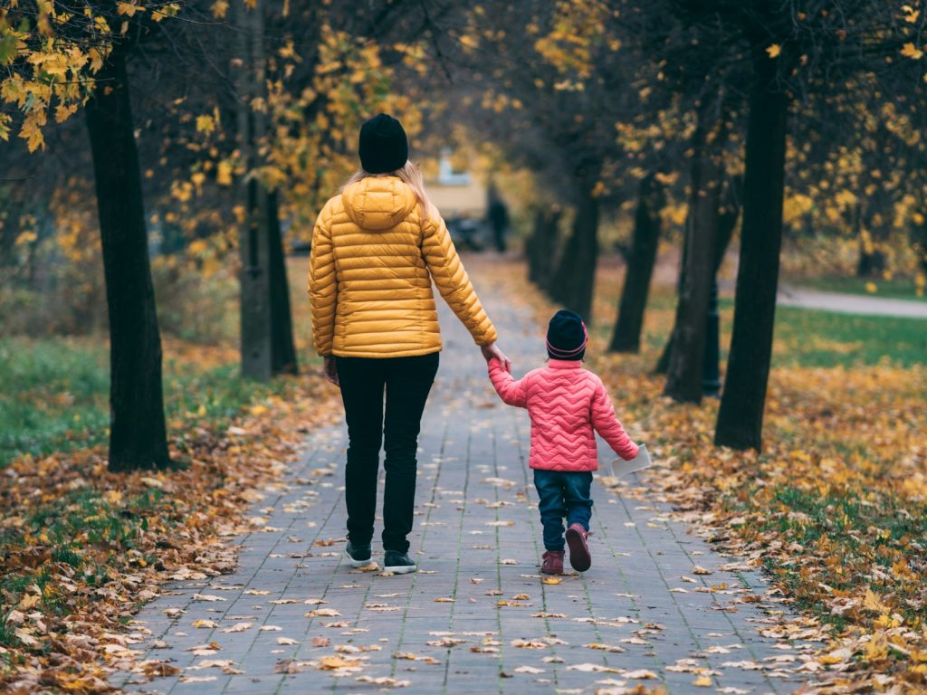 Parent and toddler walking hand in hand along an autumn path